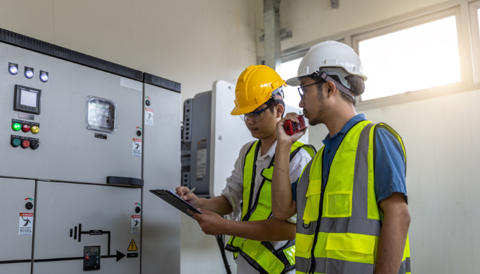 Dos ingenieros con chalecos reflectantes y cascos revisan un panel de control eléctrico, ilustrando la importancia de la Distribución Eléctrica en España y la supervisión de sistemas energéticos
