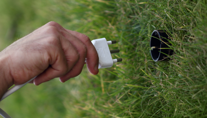 A hand plugs a three-pronged electrical cord into a grassy socket, illustrating innovative approaches to Electrical Distribution in US.