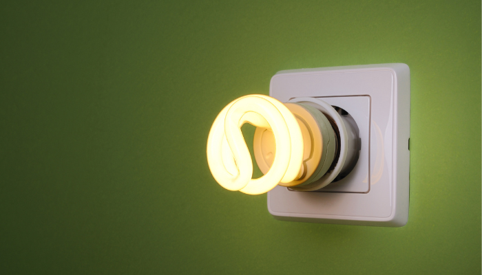 A glowing energy-saving bulb in a wall socket against a green background, symbolizing efficient solutions in the Energy Market in UK.