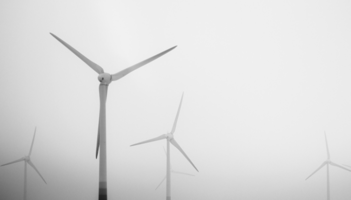 A black-and-white scene of wind turbines emerging from the fog