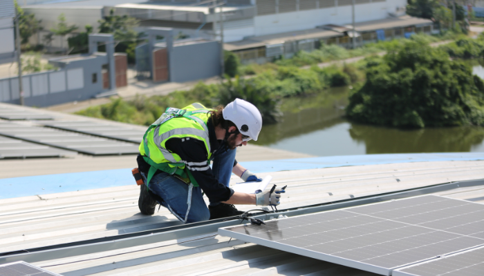 Un técnico con chaleco y casco instala componentes en un panel fotovoltaico sobre un tejado, evidenciando la adopción de Paneles Solares en España para aprovechar la energía solar.