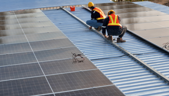 Dos profesionales con equipo de seguridad ajustan paneles fotovoltaicos en el techo de un edificio