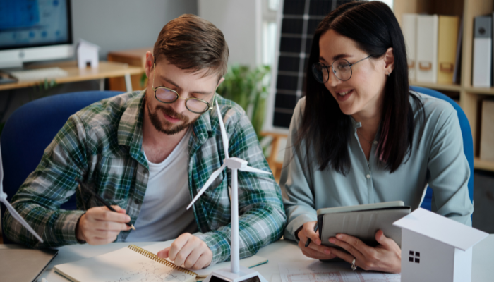 Dos profesionales trabajan en el diseño de una turbina eólica sobre la mesa, reflejando la planificación y desarrollo de Proyectos Energéticos en España.
