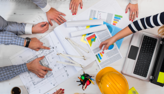 A group of professionals collaborate over blueprints, charts, and sustainability reports, symbolizing strategic planning