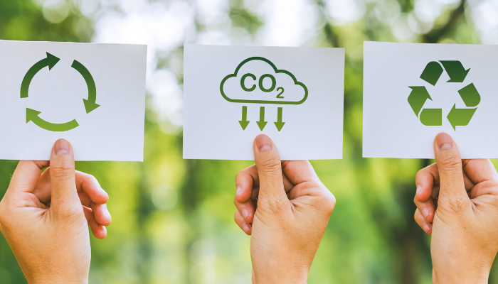 Manos sosteniendo tarjetas con símbolos de reciclaje y reducción de CO2, representando la Sustentabilidad e Innovación en Uruguay.