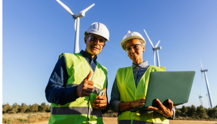 Dos profesionales con chalecos reflectantes y cascos revisan datos en un campo eólico, representando la importancia de la Sustentabilidad en España