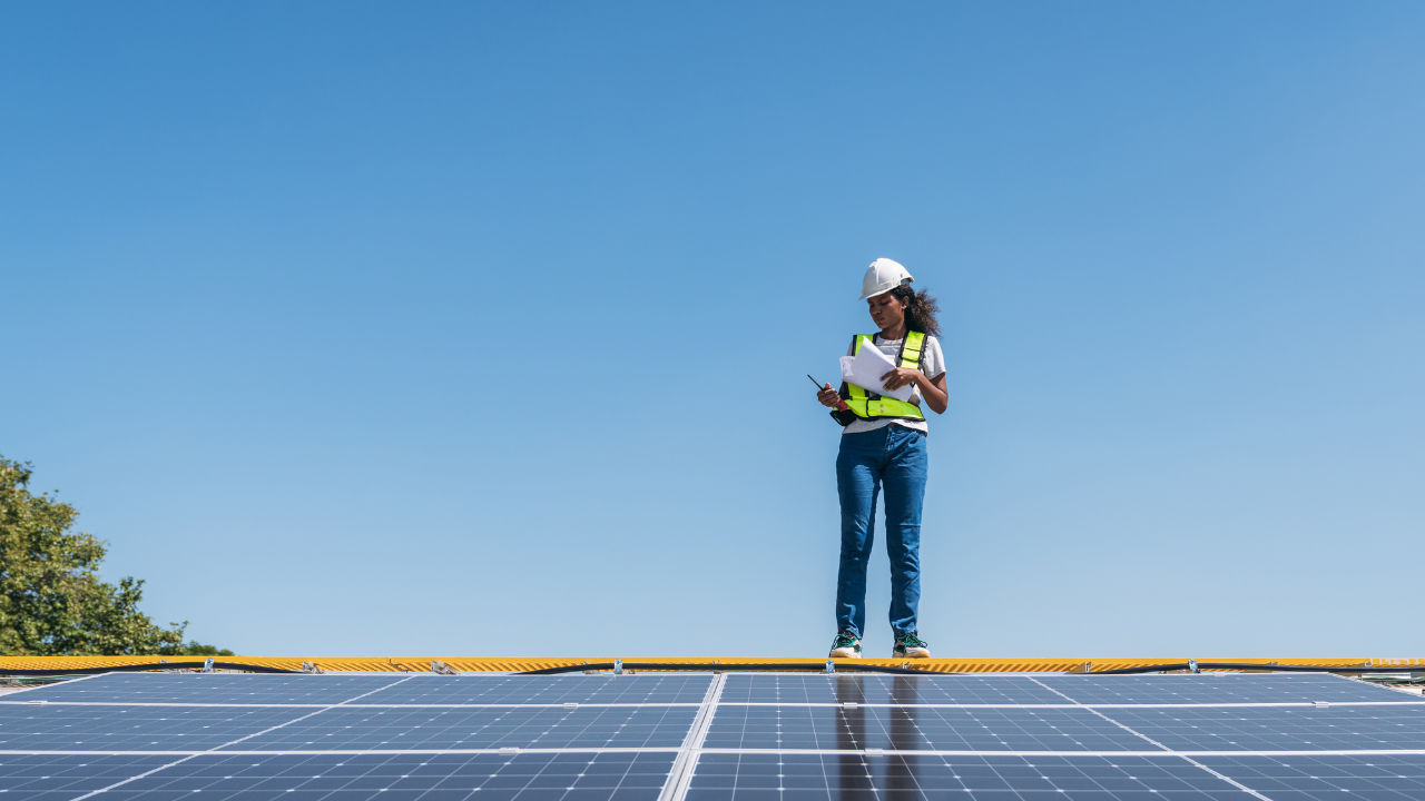 An engineer stands on top of a solar panel installation, reviewing technical documents. The image reflects the UK's focus on clean energy and professional commitment to solar self-consumption.