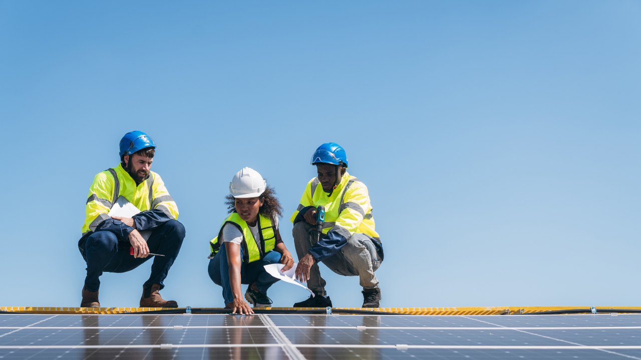 Tres operarios, dos de ellos arrodillados sobre una estructura solar, inspeccionan y revisan planos bajo un cielo despejado. Esta escena representa la implementación práctica de la Energía solar de concentración en el contexto uruguayo, con énfasis en el trabajo en equipo.