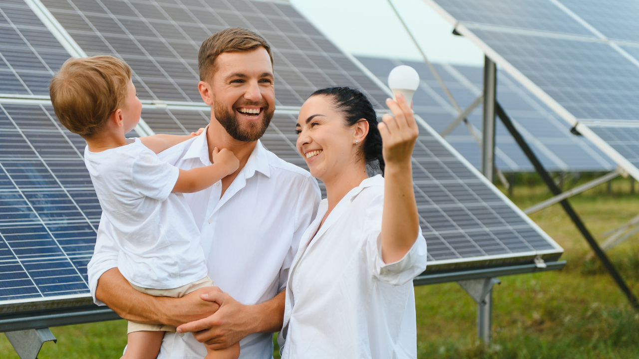 A smiling family stands near solar panels, with the mother holding an LED bulb, symbolizing clean energy. The phrase "Solar panels" reinforces the idea of sustainable living and energy independence.
