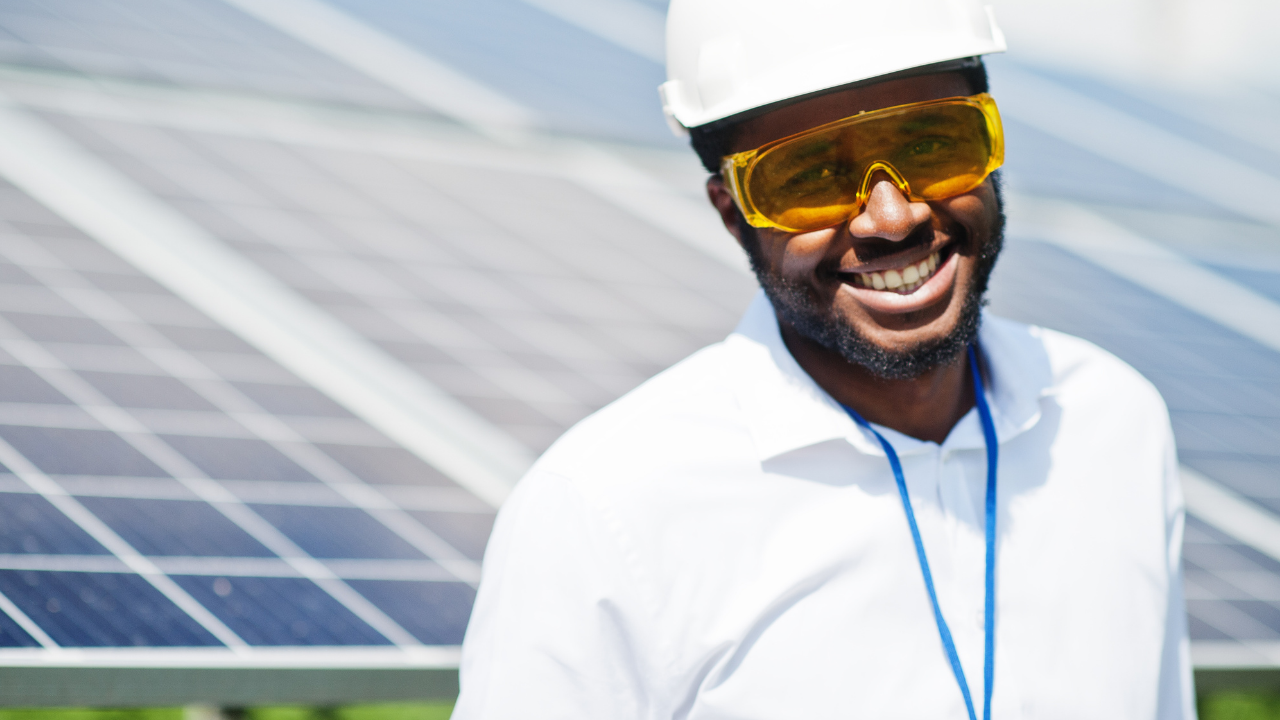 Un técnico sonriente con casco y gafas de protección está frente a paneles solares. La frase "Paneles solares" resalta el enfoque profesional en energías limpias.