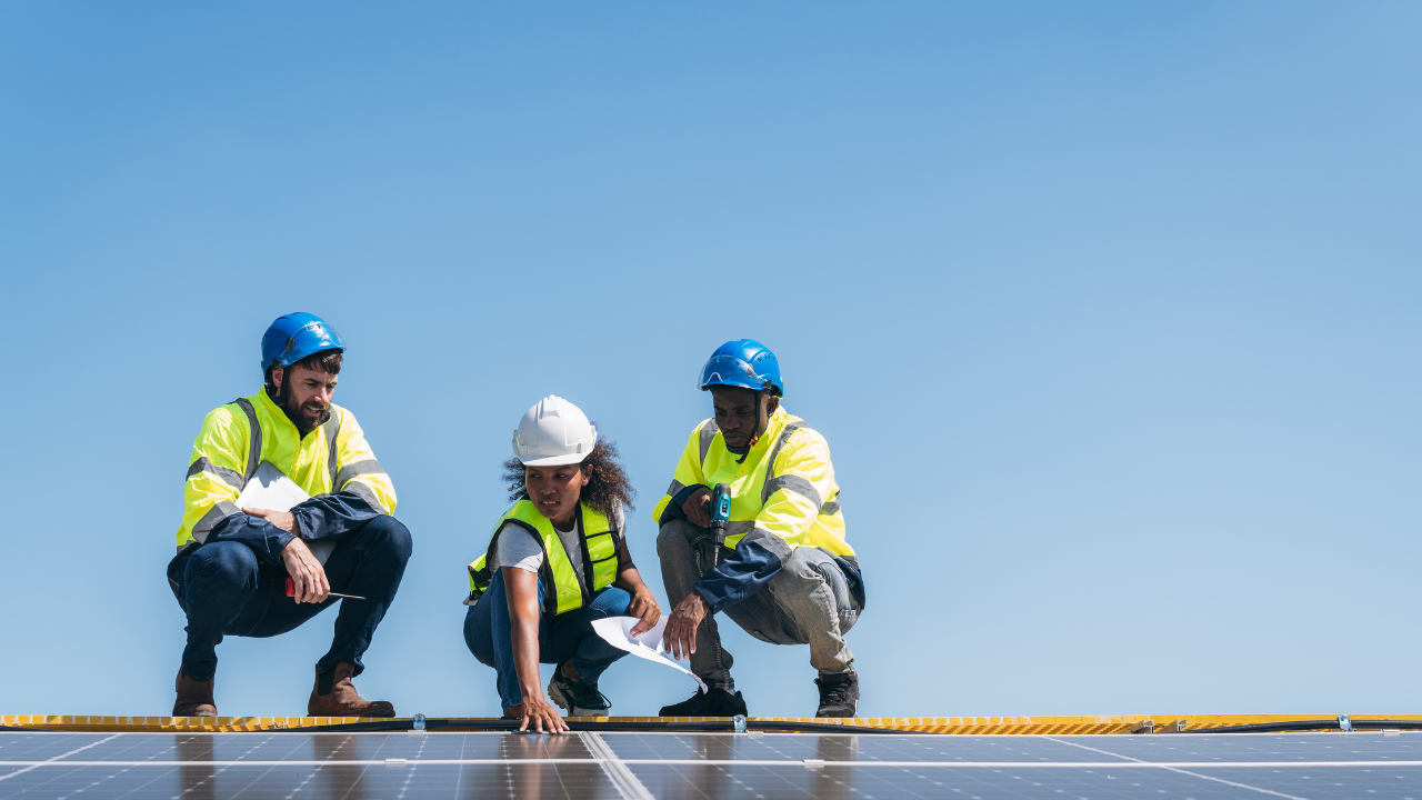 Tres técnicos inspeccionan un panel solar desde una posición elevada. Visten chalecos reflectivos y cascos, en plena actividad técnica. La escena representa la implementación práctica y colaborativa de paneles solares portátiles en el contexto argentino.