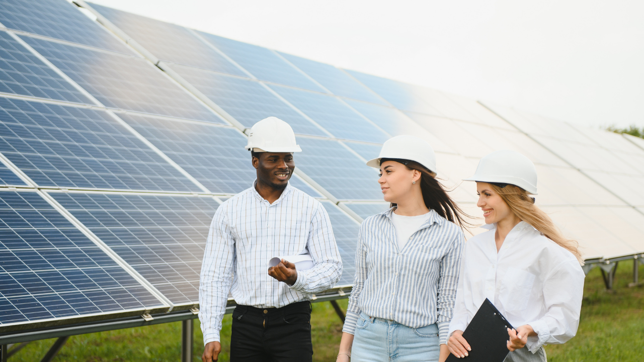 Three colleagues are walking and discussing beside solar panels. Their relaxed body language and teamwork reflect the practical implementation of shared self-consumption in a community-focused and forward-looking setting.