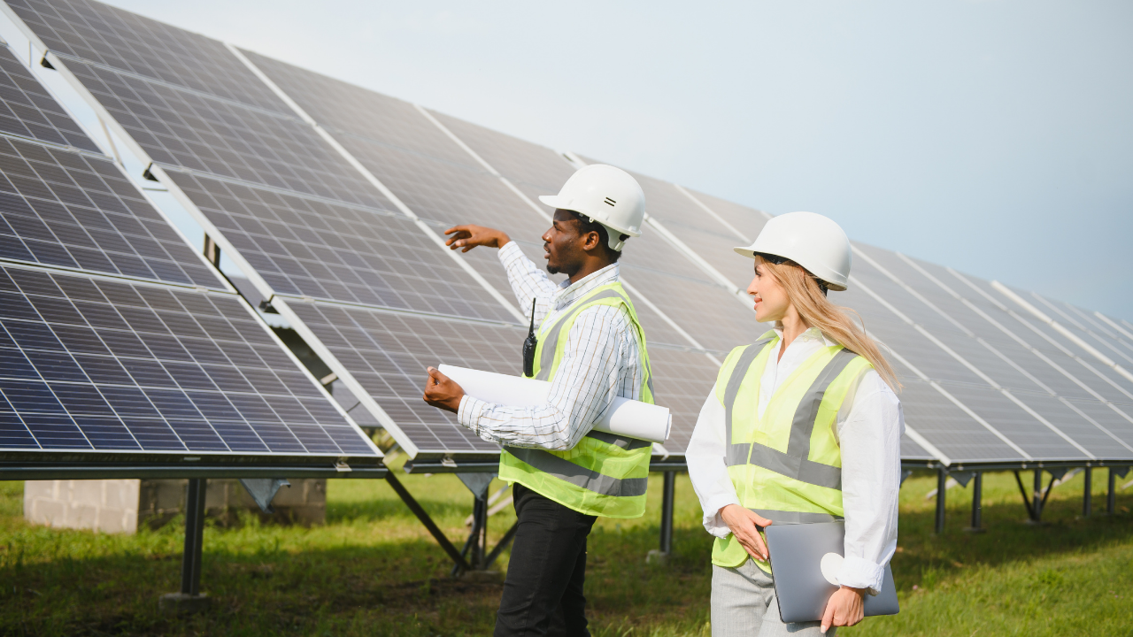 La escena muestra nuevamente a dos profesionales conversando frente a una hilera de paneles solares. La actitud colaborativa y el entorno verde reflejan el impulso uruguayo hacia energías renovables y trabajo técnico conjunto.