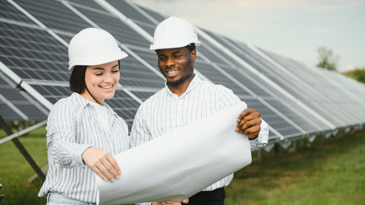 Dos ingenieros revisan planos con entusiasmo junto a una instalación solar. La escena resalta el impacto positivo de ayudas y subsidios en proyectos de energía sostenible, mostrando una colaboración técnica efectiva.