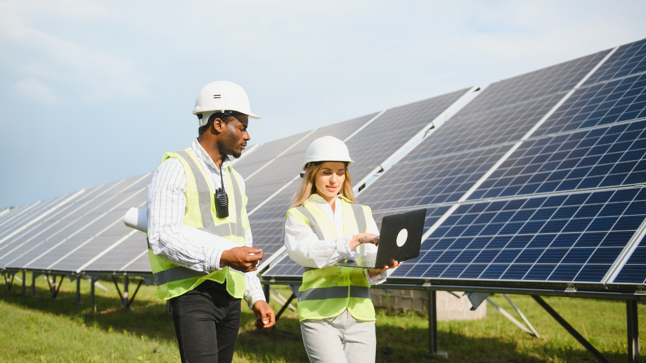 Una pareja de ingenieros revisa datos en una laptop junto a un campo de paneles solares. La imagen resalta la integración arquitectónica como proceso colaborativo que armoniza la tecnología con el entorno natural y construido.