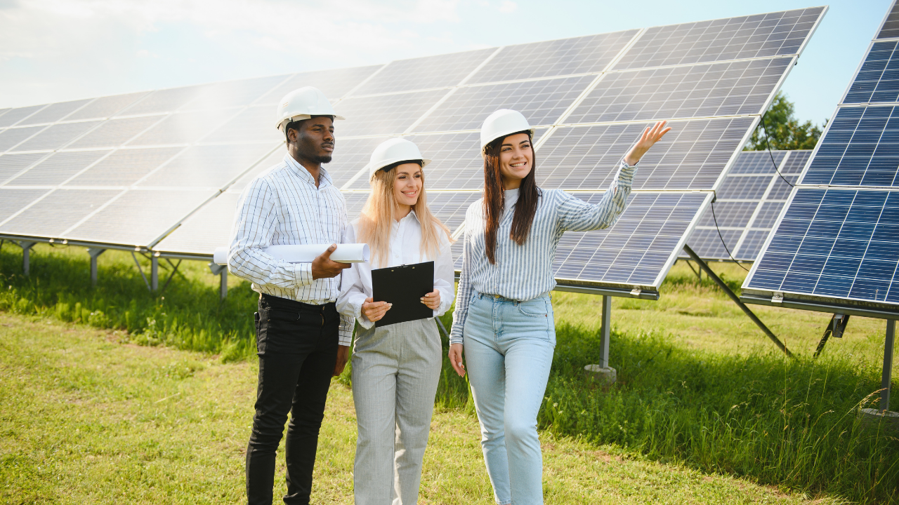 A group of three professionals, smiling and engaged, discuss solar technology while standing beside large photovoltaic panels. The image promotes teamwork and innovation in implementing solar trackers across sunny, open fields.