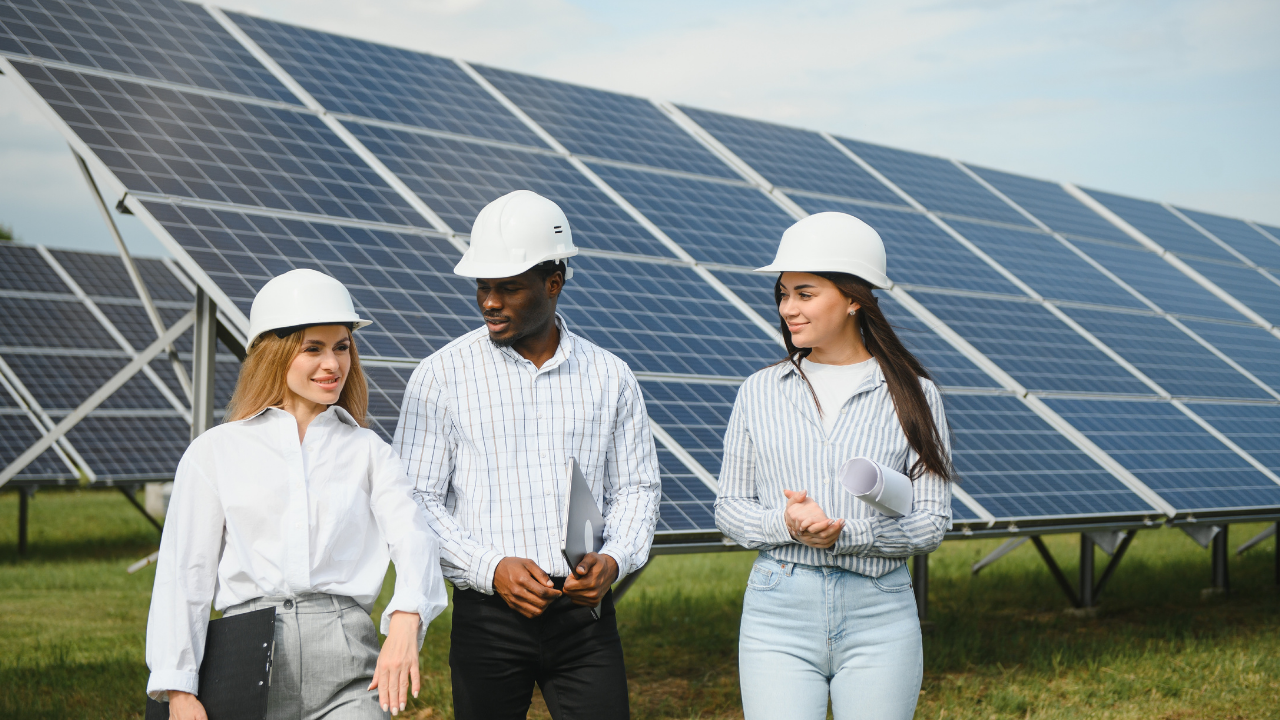 Un equipo de profesionales conversa animadamente mientras camina junto a una instalación solar. Su actitud distendida refleja colaboración en proyectos de seguidores solares con impacto sostenible.