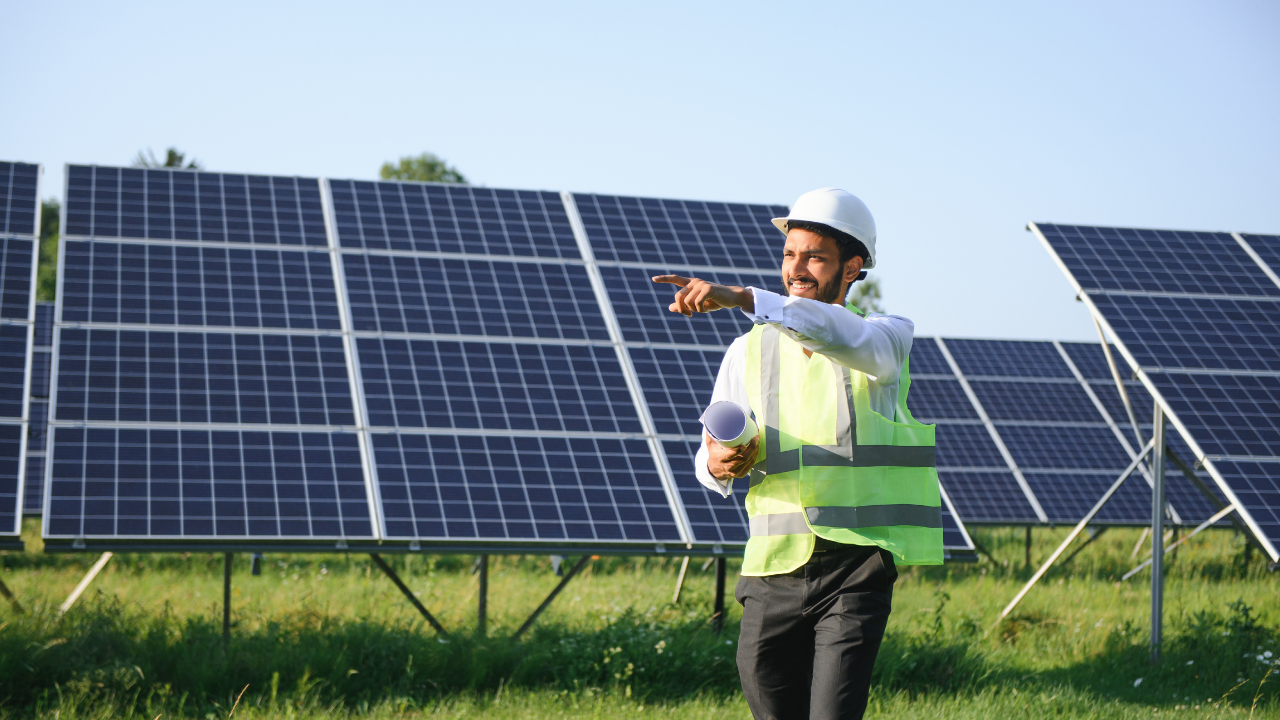 Un técnico sonriente con casco y chaleco reflectante señala hacia adelante, sosteniendo planos en una mano. La escena resalta la planificación y entusiasmo por instalar paneles solares en proyectos argentinos.