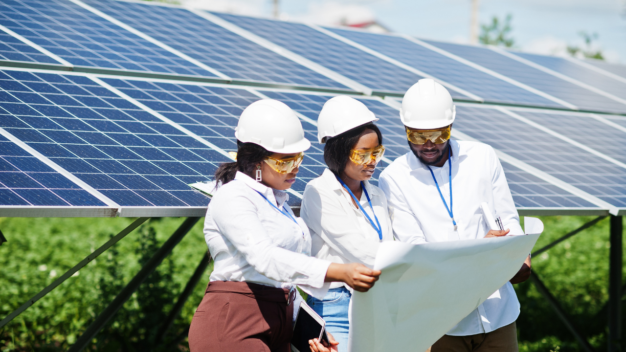 Un equipo de tres personas, con planos en mano y actitud analítica, examina un sitio de energía solar. Reflejan el proceso de diseño e implementación de baterías solares en entornos rurales para asegurar autonomía energética.