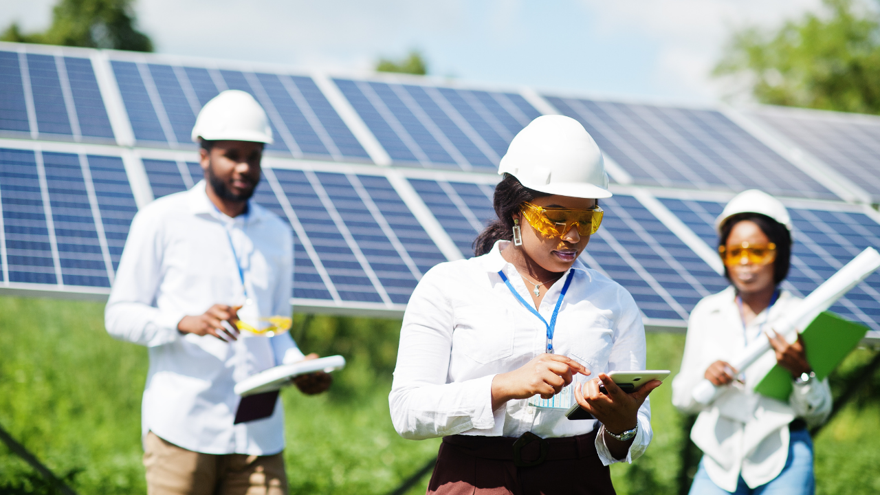 Tres técnicos trabajan coordinadamente frente a una instalación solar. Una de ellas interactúa con una tablet, lo cual muestra el monitoreo digital del sistema de paneles solares.