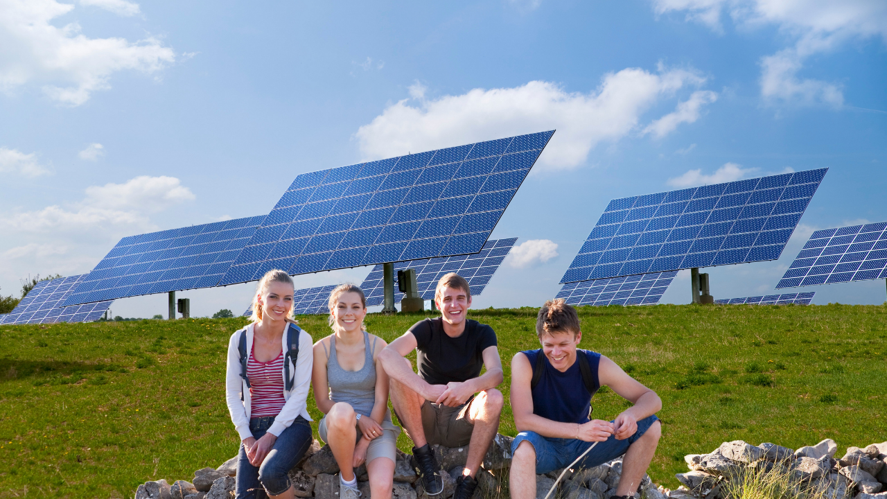 Un grupo de jóvenes sonrientes se relaja en un campo verde rodeado de paneles solares. La escena transmite una conexión positiva entre juventud y energía limpia gracias a los paneles solares portátiles.