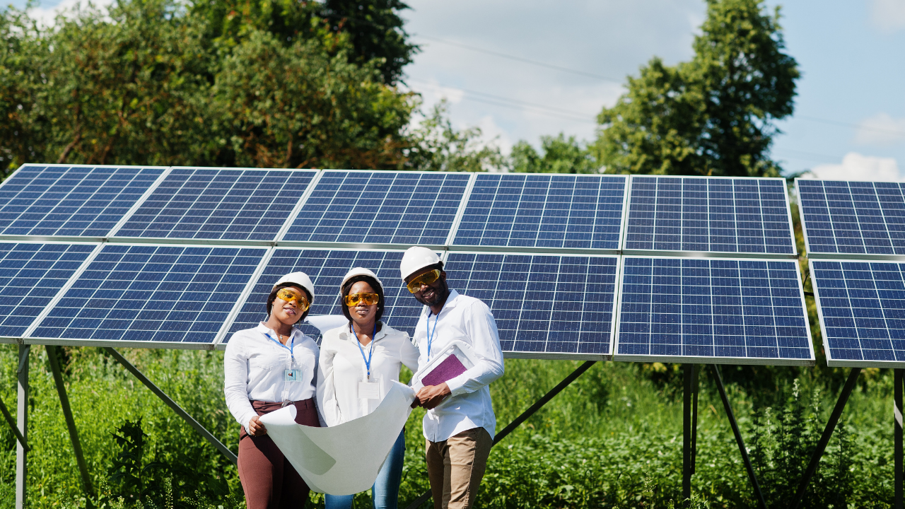 A group of three engineers stands smiling in front of a solar panel array, holding a large blueprint. Their helmets and safety glasses emphasize a professional approach to renewable energy solutions, highlighting the promise of solar thermal energy.