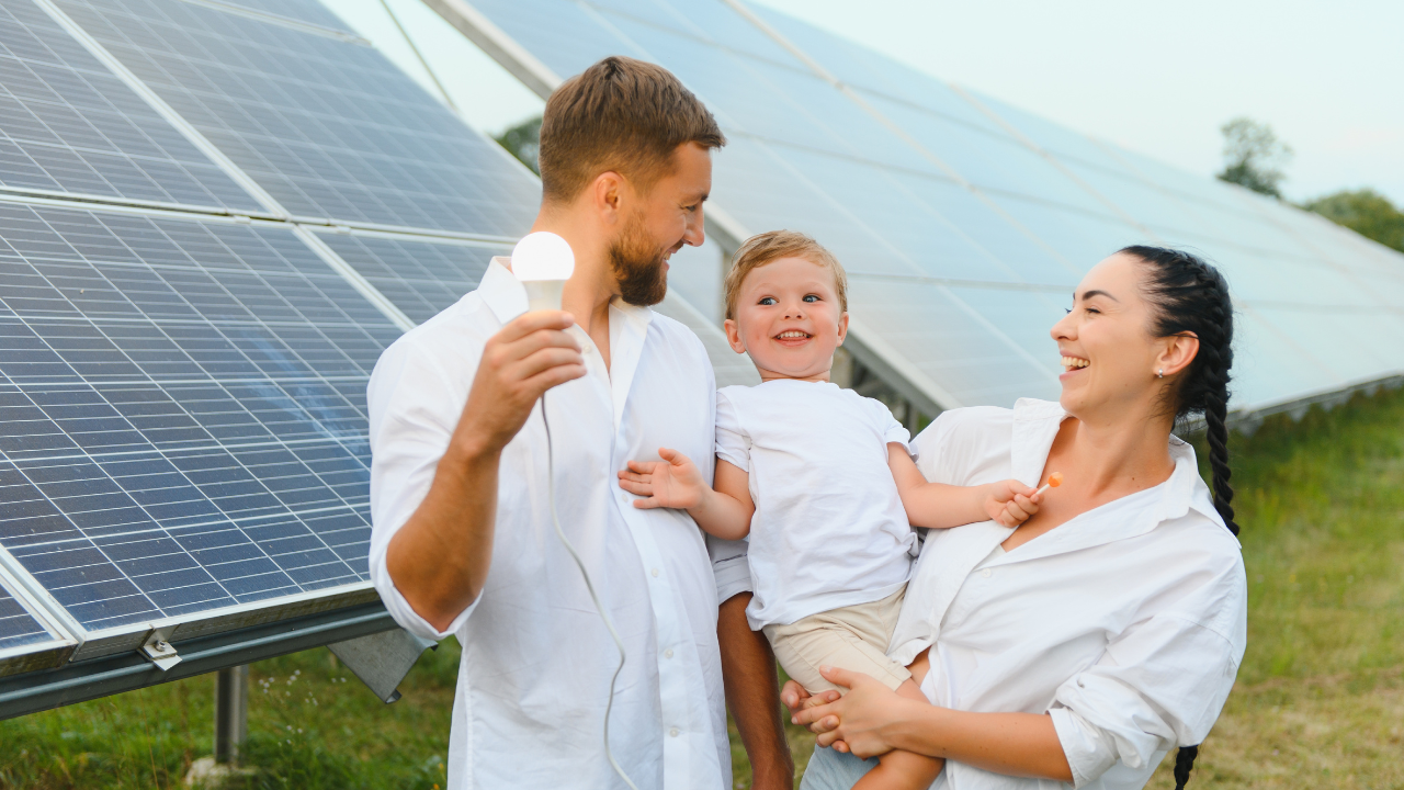 Una familia sonríe mientras el padre sostiene una bombilla conectada, enmarcados por paneles solares. Representa el impacto directo y beneficioso de instalar paneles solares en los hogares uruguayos.