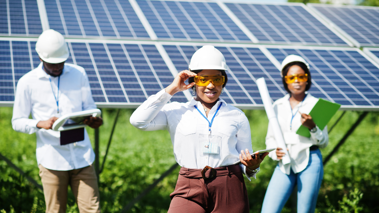 A diverse team of professionals is inspecting a field of solar panels. Wearing hard hats and safety glasses, they stand confidently in front of the technology, symbolizing the UK's commitment to clean energy and innovation.