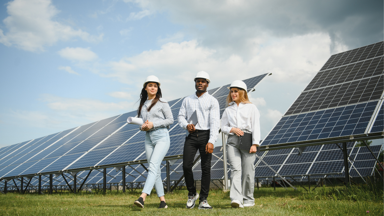 Three young engineers walk together among solar panels, showcasing a modern, collaborative approach to renewable energy in the U.S. The partly cloudy sky frames a productive day in the solar field.
