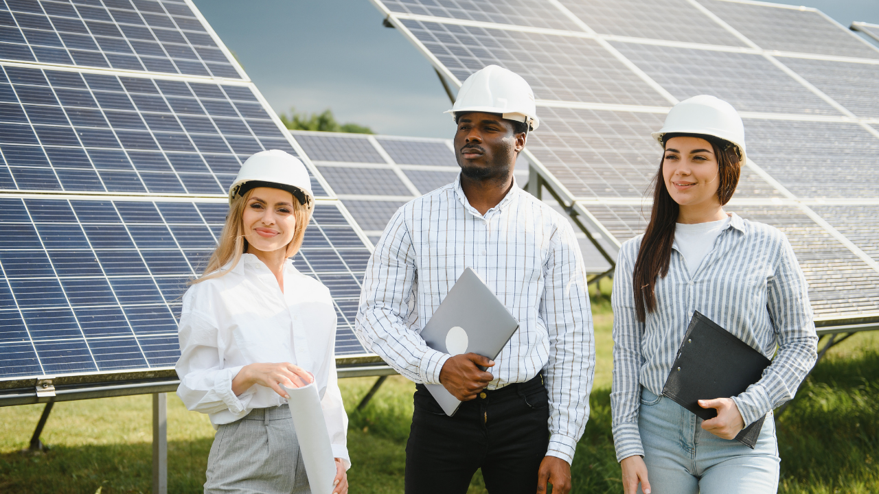 Tres personas posan frente a un conjunto de paneles solares, sonriendo y equipadas con elementos técnicos. Su postura transmite orgullo y profesionalismo en el desarrollo de energías limpias en el contexto argentino.