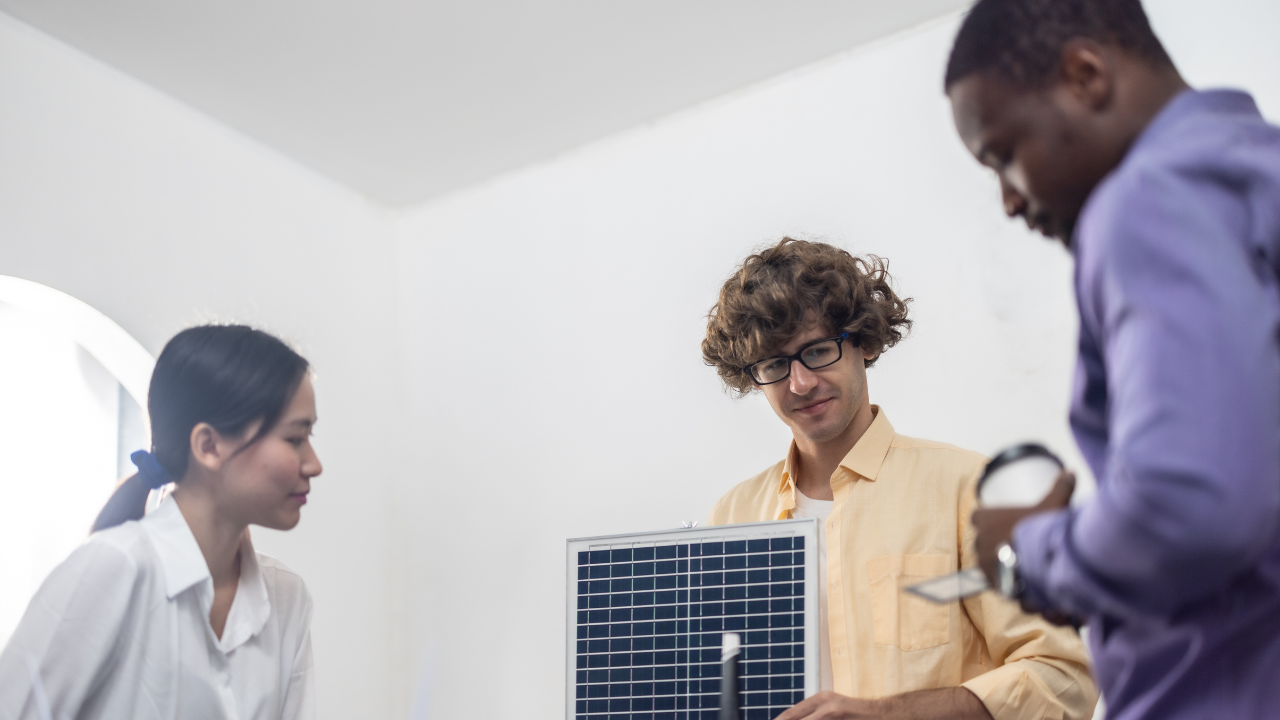 Un grupo de personas en una oficina observa con atención un panel solar pequeño, simulando una instalación doméstica. Refleja el interés creciente por instalar paneles solares en casa.