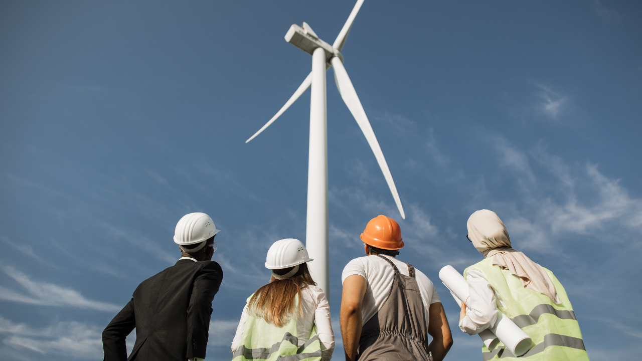 Un equipo multidisciplinario observa una turbina eólica, evidenciando análisis técnico y planificación en la producción eficiente de energía.