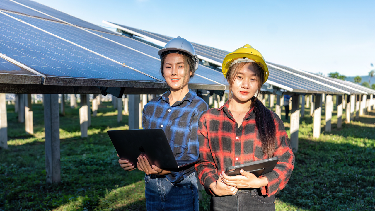 Two female engineers pose in front of solar panels with tablets and a laptop, symbolizing technological integration and women's empowerment in the American energy sector linked to solar self-consumption.
