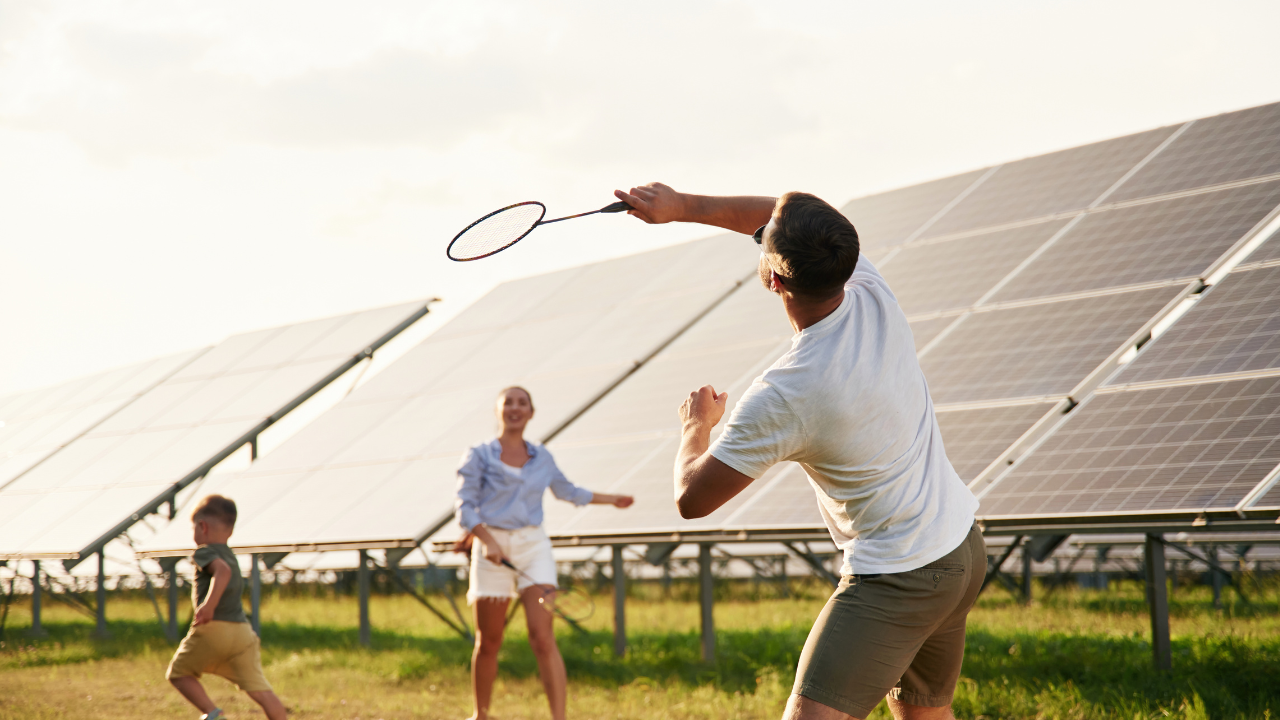A family enjoys a game of badminton beside a large solar installation. This relaxed and lifestyle-focused portrayal aligns with the American vision of integrating solar energy for businesses into everyday life and recreation.