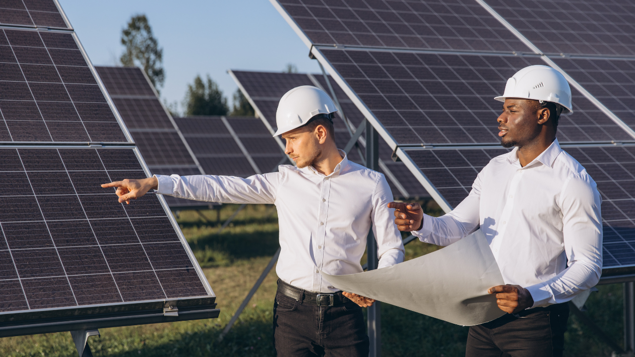 Two men in white shirts and helmets examine and point at solar panels, conveying precision and planning in a U.S. solar energy site.