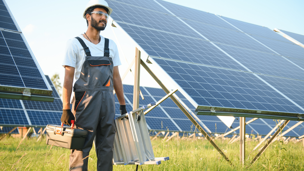 Un trabajador con herramientas y escalera camina junto a una instalación de paneles solares, destacando el rol técnico y la dedicación en proyectos solares uruguayos.