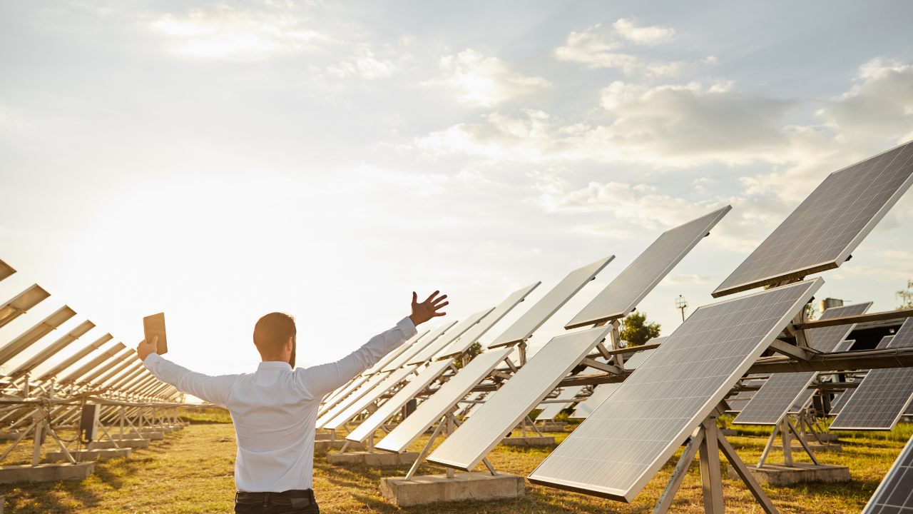 A man raises his arms toward the solar field with enthusiasm, celebrating the role of clean technology in minimizing the Carbon footprint across expansive American installations.