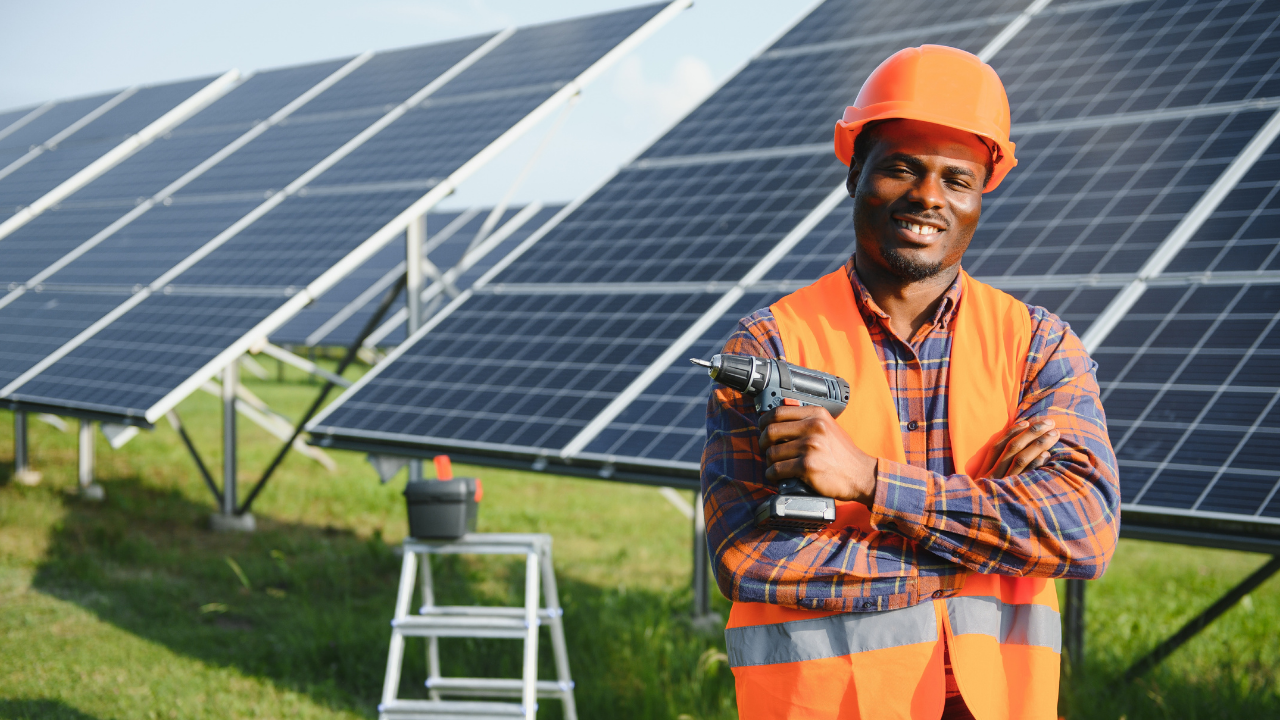 Un trabajador posa con herramientas frente a paneles solares, transmitiendo orgullo por su rol activo en la lucha contra la huella de carbono a través de la energía renovable.