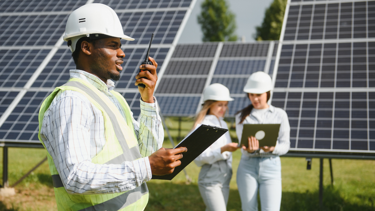 Un ingeniero habla por radio mientras coordina con dos colegas que analizan datos en una laptop, todo en un entorno de paneles solares. Representa la colaboración y profesionalismo argentino en la implementación de energía solar en empresas.