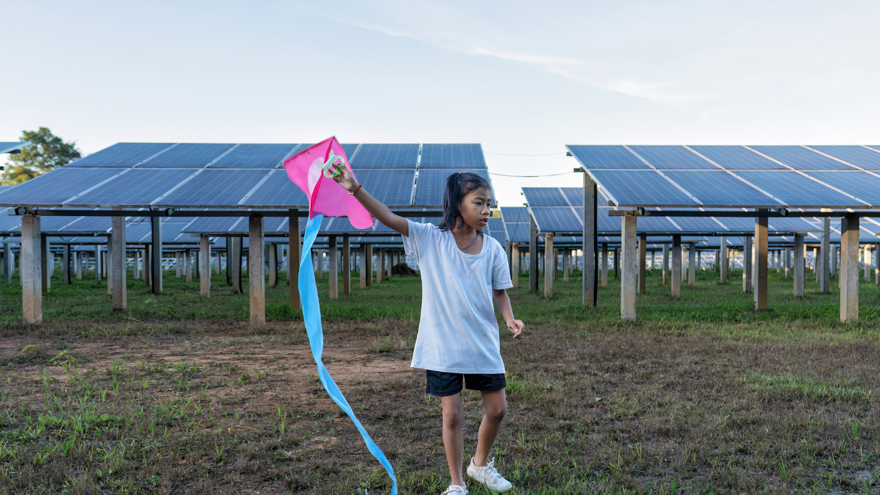 A girl holds a colorful kite near rows of solar panels, highlighting the harmony between green energy and carefree childhood in an American solar park.