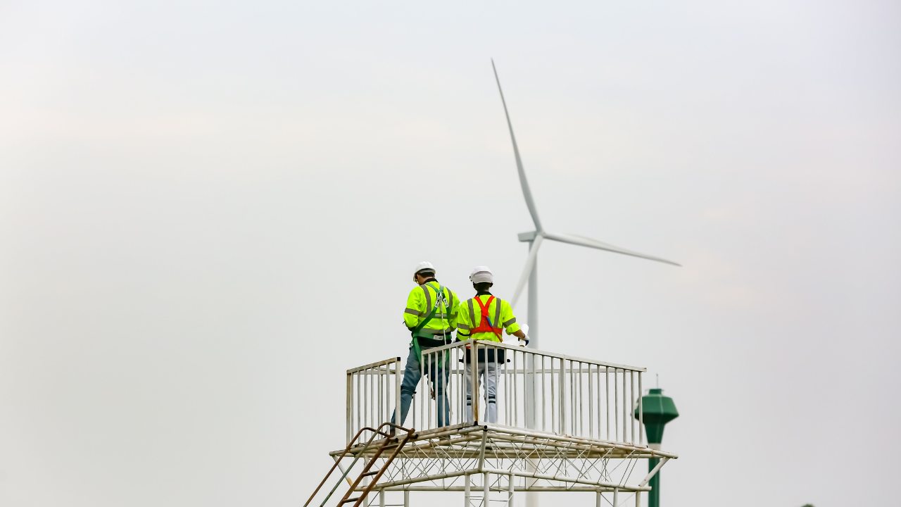 Dos técnicos observan una turbina desde una plataforma elevada, supervisando el proceso de integración eólica en un parque argentino.