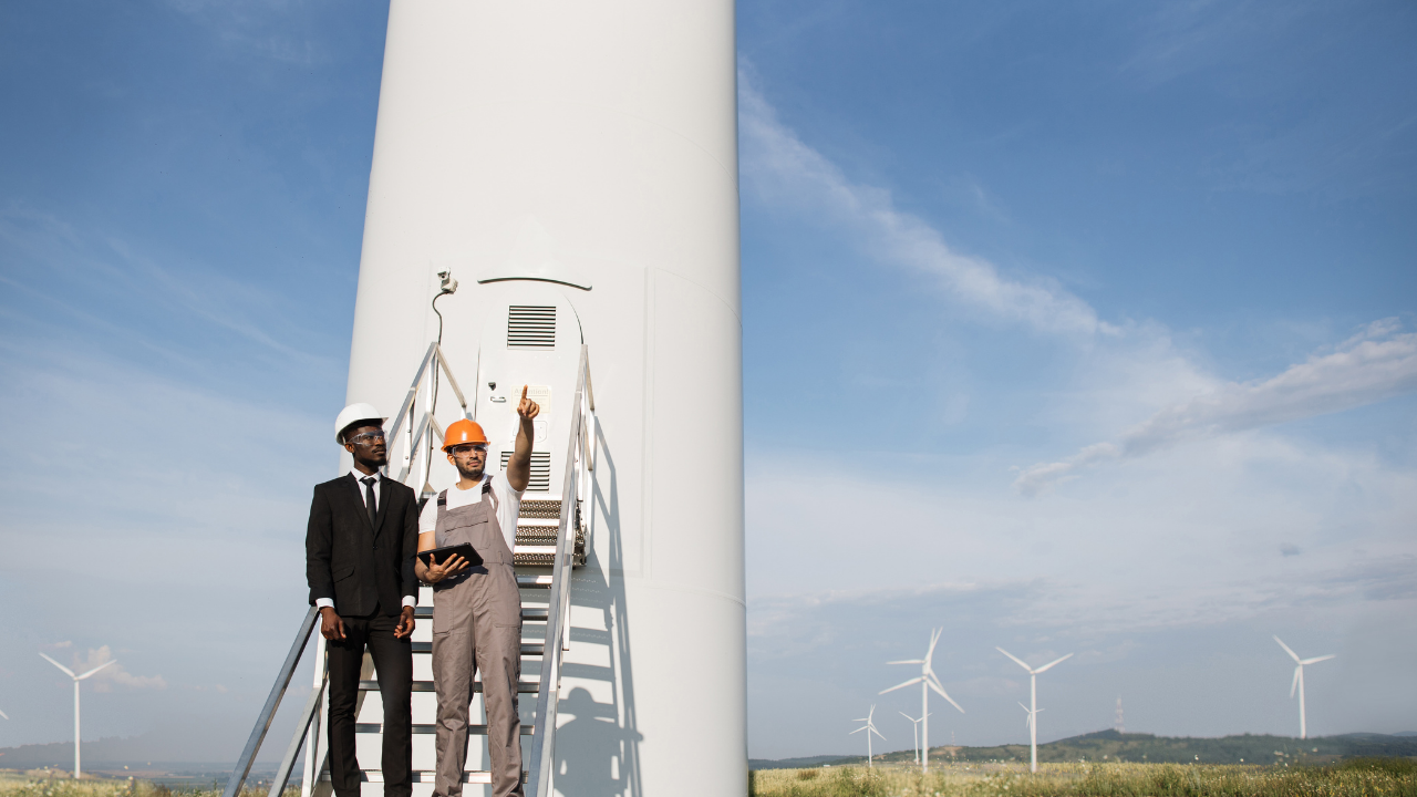 Un ingeniero con traje y otro con mono de trabajo analizan una torre de turbina, simbolizando la colaboración entre gestión y operación en la integración eólica española.