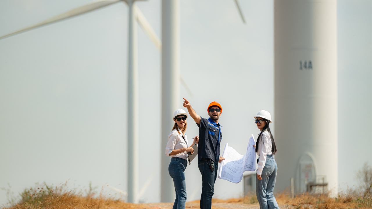 A team of professionals examines architectural plans among wind turbines in a semi-urban setting, illustrating the UK’s commitment to urban wind turbines.