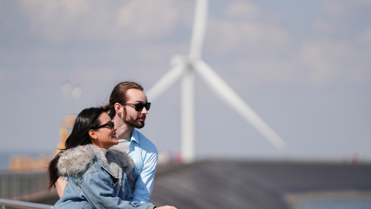 A couple enjoys the view near a coastal wind turbine, representing how urban wind turbines blend with public and recreational spaces in the U.S.