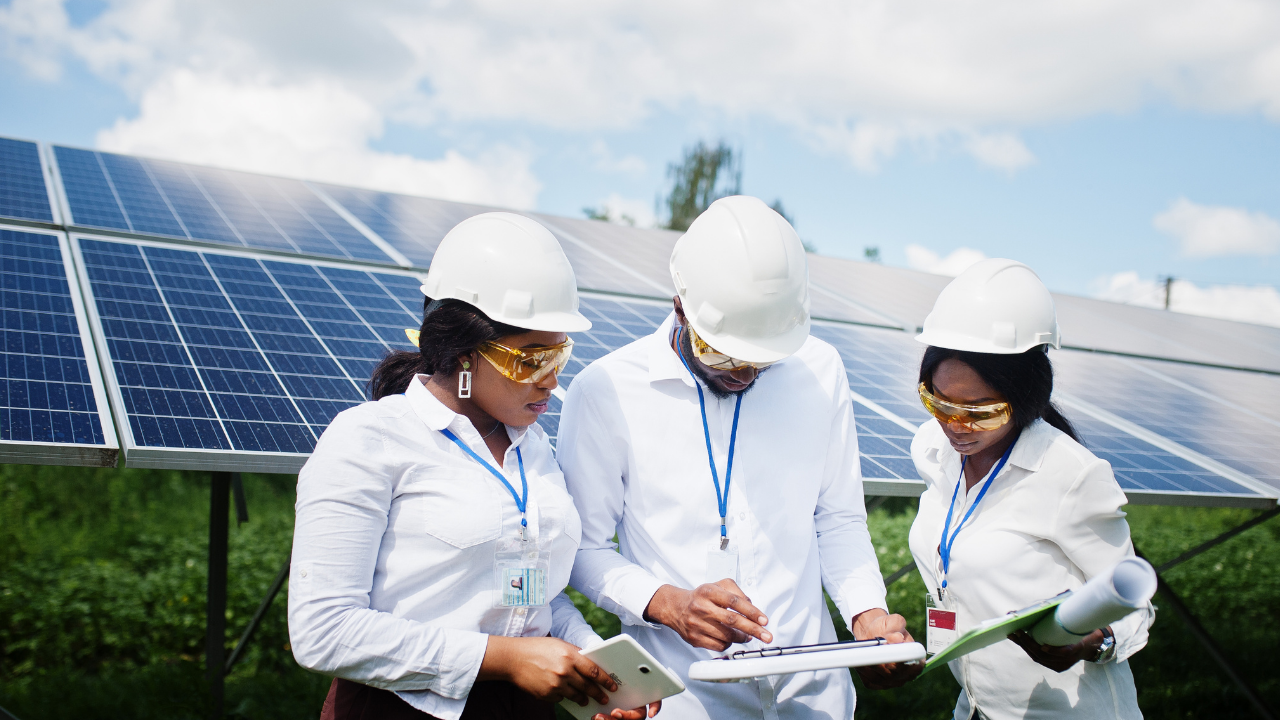 A team in helmets and safety glasses reviews documents in front of solar panels, highlighting detailed planning to maximize return on investment in American solar projects.