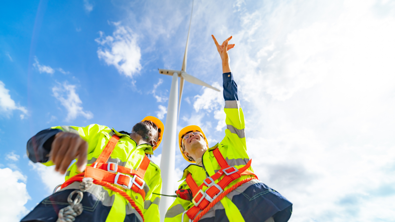Dos trabajadores observan hacia arriba junto a una torre eólica, evidenciando el enfoque técnico español en la expansión de aerogeneradores urbanos.