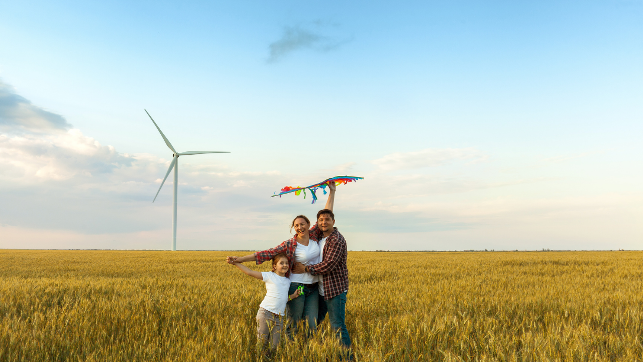 Una familia sonriente en un campo de trigo posa con una cometa frente a un molino de viento, transmitiendo armonía entre naturaleza y tecnología.