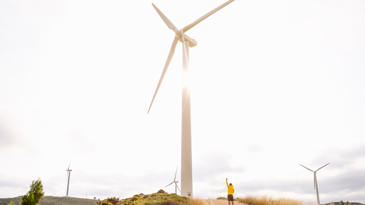 Un técnico argentino levanta la mano frente a una turbina gigantesca, destacando la escala de los aerogeneradores y su relación con el impacto ambiental local.