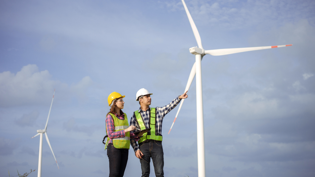 Two technicians examine a wind turbine closely, discussing operational details as part of routine wind turbine maintenance in the UK.