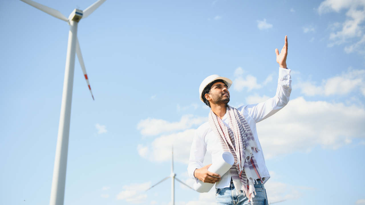A wind energy engineer gestures towards a turbine on a bright day, symbolizing the UK's forward-looking investment in renewable energy.
